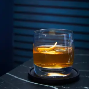 Rocks cocktail glass with whiskey and lime shown on a blue bar
