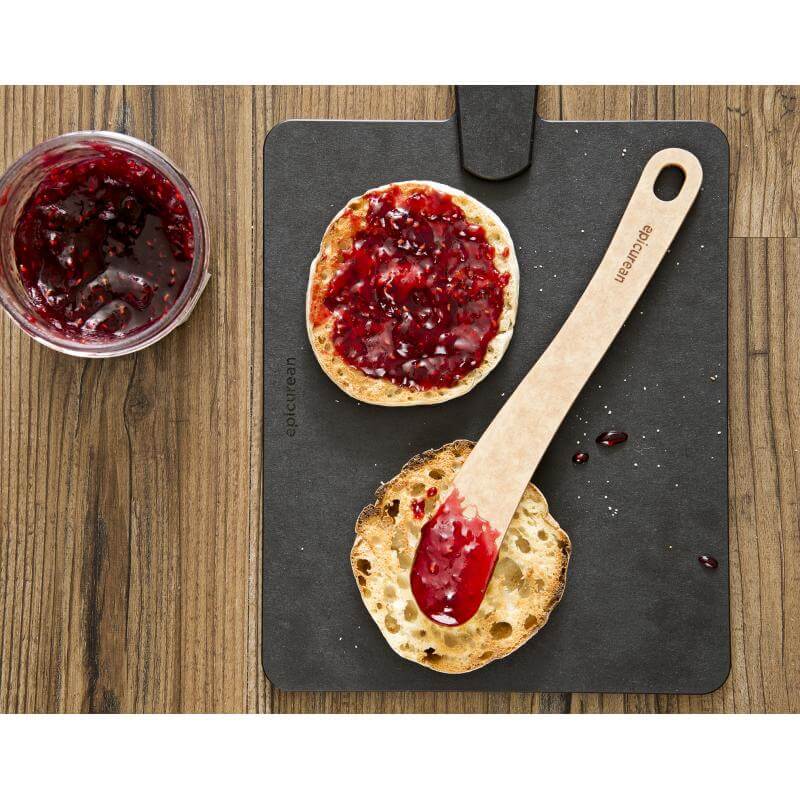 Epicurean spreader shown with English muffin and jam on a cutting board on brown table