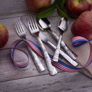 Liberty 5 piece place setting flatware shown on a wood table with apples and USA ribbon.