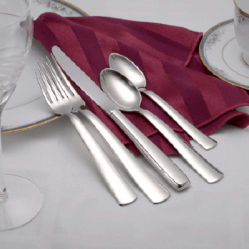 Modern America plain shiny 5-piece place setting flatware shown on a white tablecloth and red napkin.