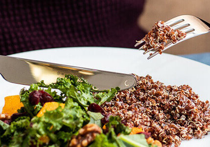 Salad with quinoa on white plate with fork and knife.